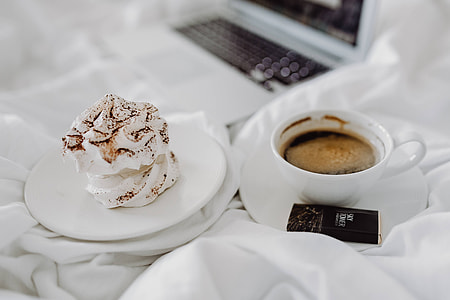 Woman working on a laptop while enjoying a breakfast coffee and chocolate in bed thumbnail