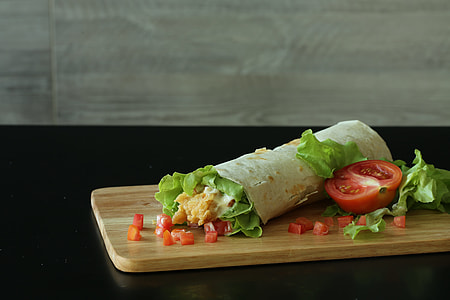 wrapped food with tomatoes and lettuce on brown wooden chopping board thumbnail