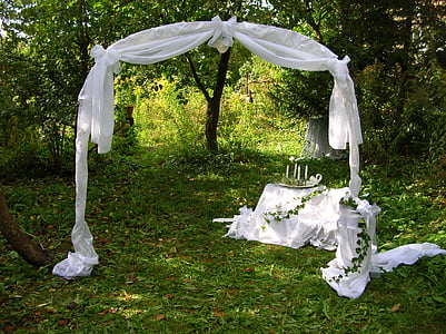 white wedding archway surrounded by green leaf trees thumbnail