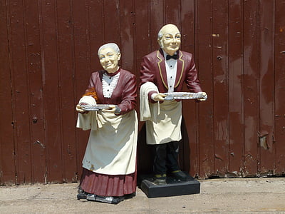 waiter and waitress statues beside brown fence thumbnail