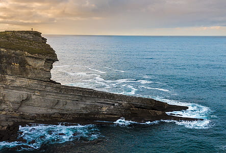 gray concrete rock near ocean during cloudy skies thumbnail