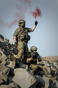 man standing on rocks while holding red smoke grenade beside man sitting on rocks thumbnail