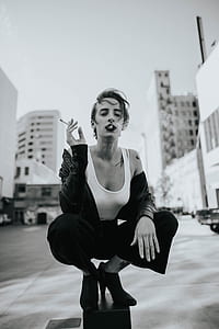 grayscale photography of woman holding cigarette stick while sitting on black stand thumbnail