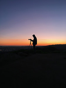 silhouette photo of a man standing at the peak of the mountain using DSLR camera thumbnail