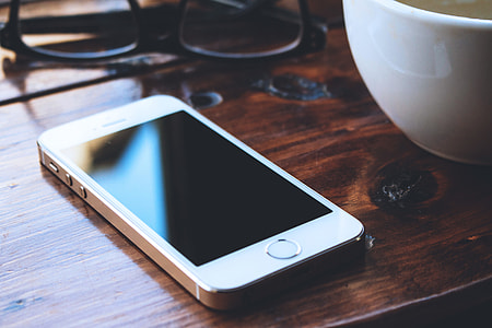 Glasses, coffee cup and white iPhone mobile on table thumbnail