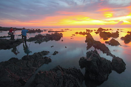 2 People Standing on Rock Formation Reflected on Water during Sunset thumbnail