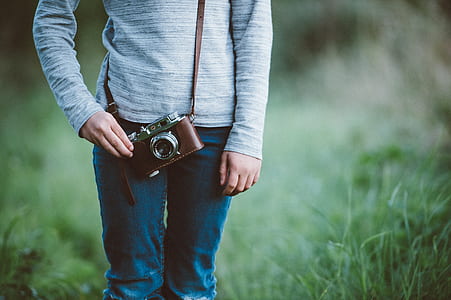 person standing on green grass field while carrying brown and gray camera thumbnail