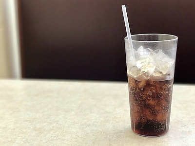 clear plastic drinking cup half-filled with black liquid and ice on white wooden table thumbnail