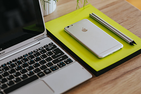 Silver Acer laptop, a white Apple iPhone and a notepad on a wooden desk thumbnail