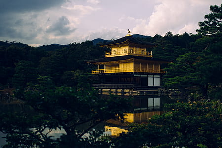 gold and brown pagoda temple surrounded with green trees under white clouds thumbnail