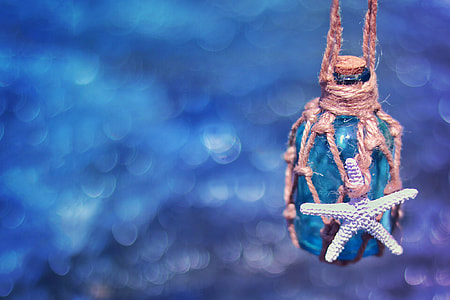 brown glass bottle wrapped in brown twine with white starfish suspended on air below blue surface thumbnail