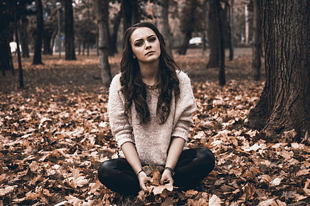 woman in gray sweater and black pants sitting on ground full of leaves thumbnail
