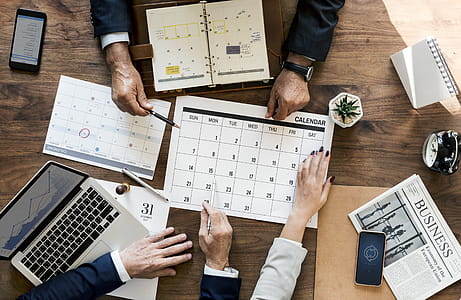 Two Men Holding Pen and Calendar Sitting Beside Table thumbnail