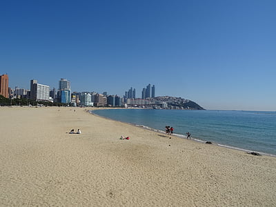 people walking on seashore near highrise building under calming sky thumbnail