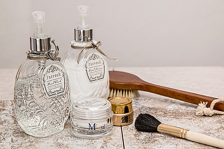 close-up of two fragrance bottles, makeup brush, and face powder on beige surface thumbnail