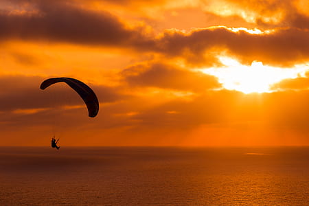 person parachuting on sea during golden hour thumbnail
