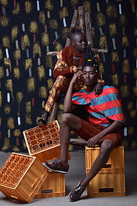 Man in Brown Shorts Sitting Beside Woman in Orange Jumpsuit on Yellow Plastic Crates thumbnail