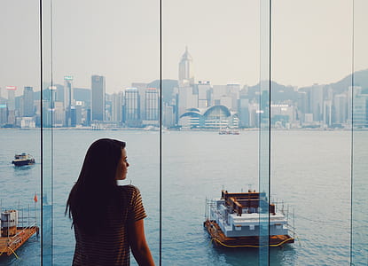 woman standing in front of clear glass wall with view of body of water and cityscape during daytime photo thumbnail