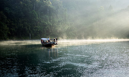 black boat filled with people on blue ocean water surrounded by green leafed trees during daytime thumbnail