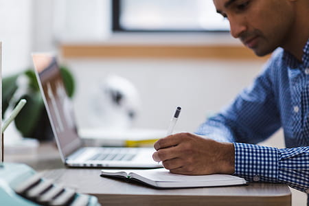 man in plaid dress shirt writing on the desk thumbnail