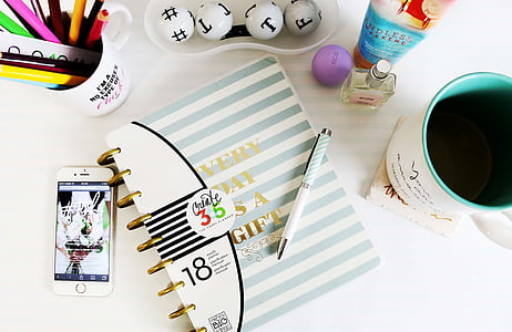 high angle photography of pen on top of book beside iPhone, mug, and fragrance bottle thumbnail
