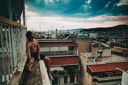 man sitting on building while looking at cloudy sky thumbnail