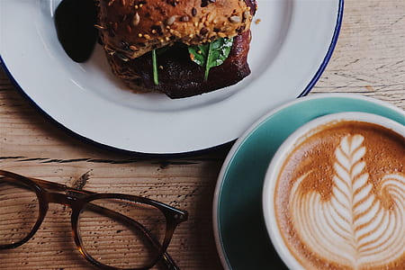 burger on white plate beside brown framed eyeglasses and coffee thumbnail