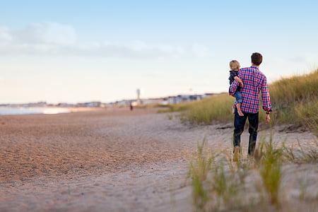 man carrying child near green grasses during daytime thumbnail