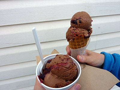 person holding chocolate flavor ice cream on cone and cup besides white wooden wall thumbnail
