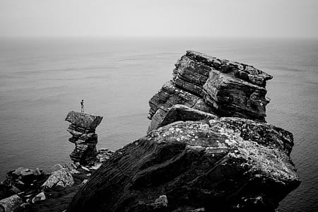 grayscale photo of man standing on rock formation thumbnail