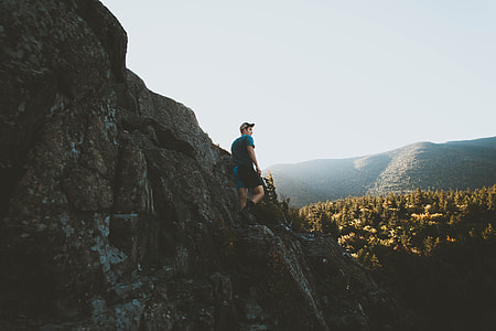 man standing on rock formation near forest thumbnail