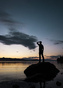 silhouette photo of man standing on rock in the middle of body of water thumbnail