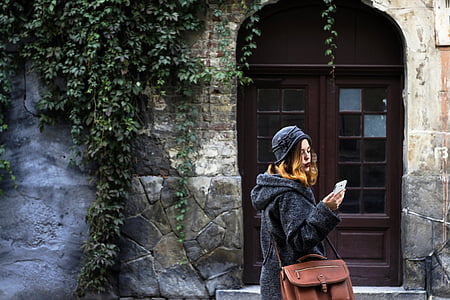 standing woman while looking at her smartphone in front of doorway thumbnail