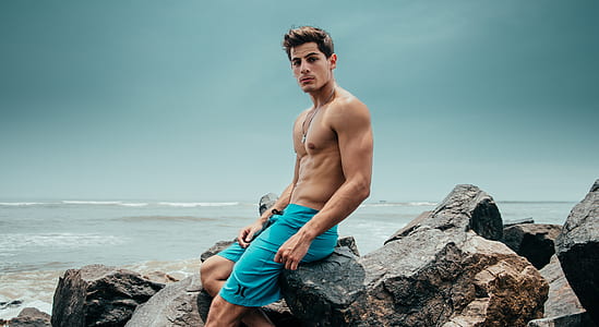 man sitting on rock near body of water thumbnail