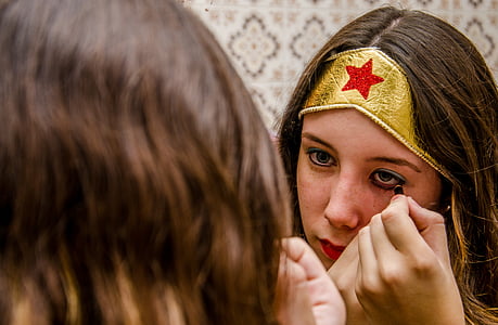 brown haired woman in front of mirror putting eyeliner makeup thumbnail