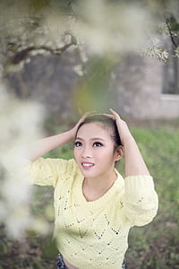woman in yellow sweater holding her head while looking on flower thumbnail