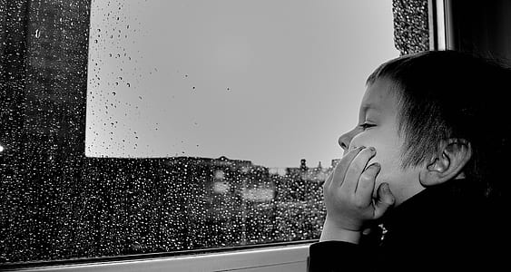 grayscale photography of boy watching the rain on window thumbnail