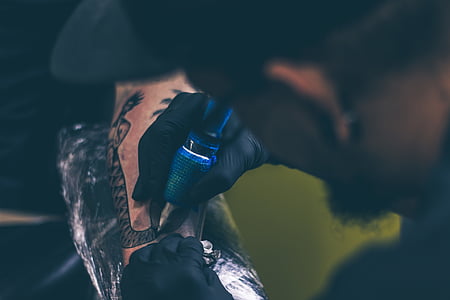 man tattooing person's arm with mermaid thumbnail