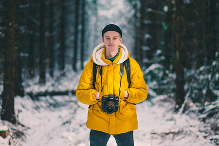 man standing hands put in yellow jacket near trees cover with snow thumbnail