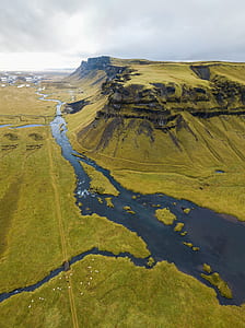 aerial photography of green grass field with lagoon and mountain under white cloudy sky at daytime thumbnail