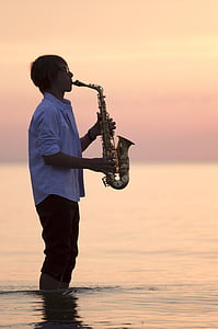 man playing saxophone standing on body of water during golden hour thumbnail
