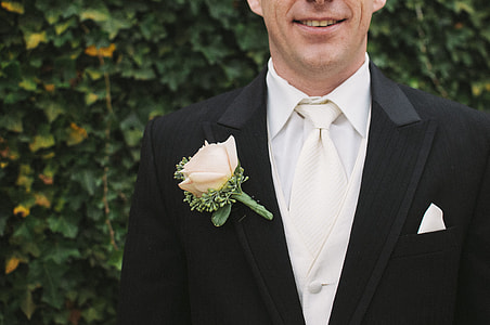 man wearing black and white suit while standing near green leafed wall thumbnail