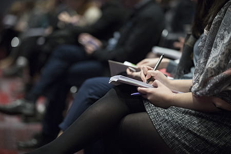 woman wearing gray sweater writing on notebook while thumbnail