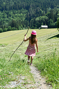 girl holding stick walking between green grass at daytime thumbnail
