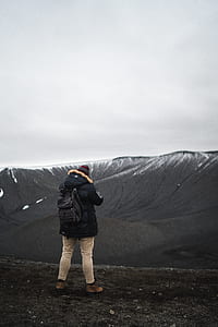 person wearing black jacket and beige pants standing on rough terrain with view of mountains photo thumbnail