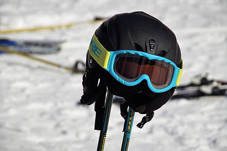black and blue ski goggles and helmet on ski poles thumbnail