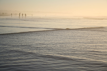 several person standing on shoreline near body of water while raining during golden hour thumbnail