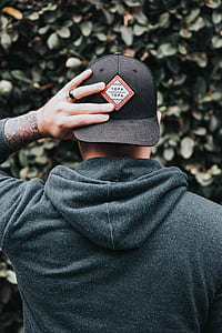 man wearing black fitted cap and hoodie holding his cap\ thumbnail