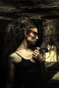 black and brown haired woman in black spaghetti strap top posing in abandon building with moth in her hand thumbnail