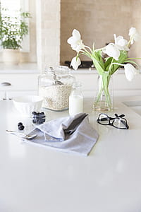 white flowers in clear glass vase beside milk and eyeglasses on white surface thumbnail